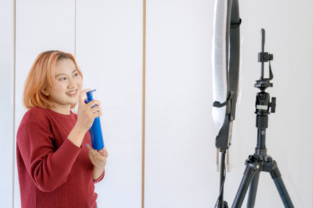 Young Asian woman social media influencer live streaming selling body lotion online with smartphone