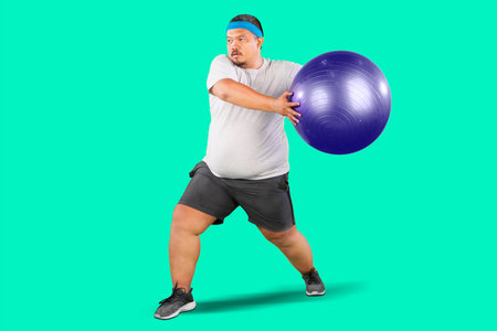Overweight Man doing fitness exercise on pilates ball isolated on green backgroundの写真素材