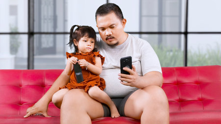 Father and daughter watching online video streaming on a mobile phone at homeの写真素材