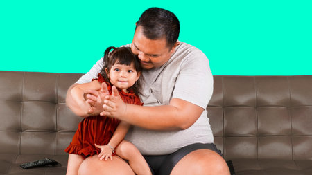 Overweight Asian man clapping hand at home with his little cute girl isolated over green backgroundの写真素材