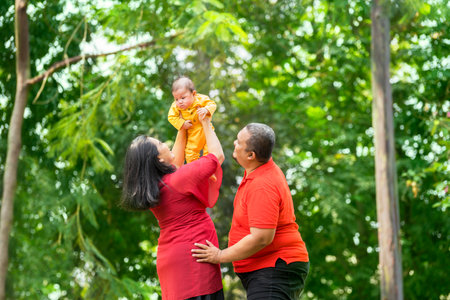 Happy asian family in the garden. Mother lifting her baby boy while father laughingの写真素材