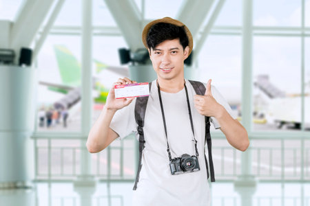 Happy Tourist at the Airport Holding Boarding Pass and Camera, Ready for Travelの写真素材