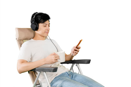 oung man relaxing with headphones, drinking coffee, and using smartphoneの写真素材