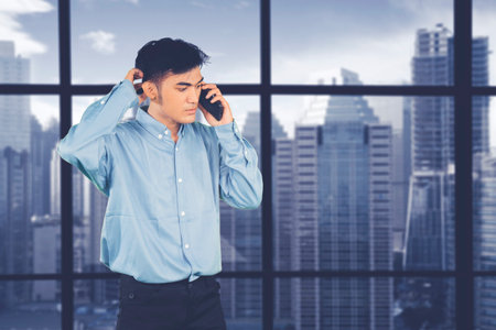 Stressed Businessman Talking on Phone with Cityscape Backgroundの写真素材