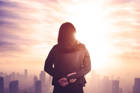 Businesswoman Overlooking City Skyline at Sunrise with Inspirational Ambianceの写真素材