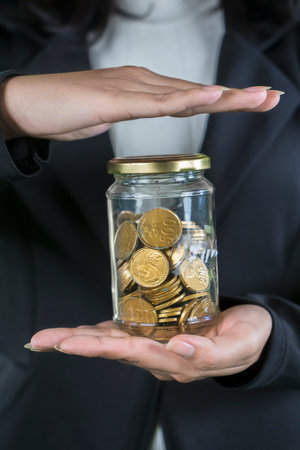 Close-Up of Hands Holding and Covering a Jar Filled with Gold Coins