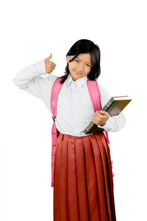 Confident Asian Schoolgirl Holding Books and Showing Thumbs Up Gestureの写真素材