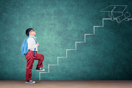Student Climbing Chalk Staircase Toward Graduation Cap on Green Blackboard Backgroundの写真素材