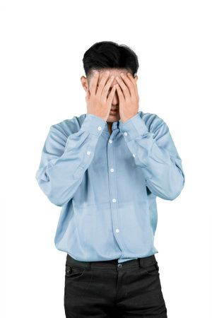 Frustrated young Asian man covering face with hands, stress and emotional pressure concept, isolated on white backgroundの写真素材
