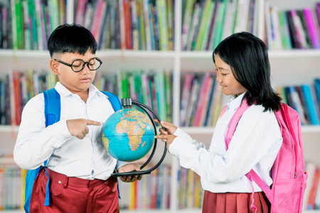 Asian school children studying a globe in the library, learning about geographyの写真素材
