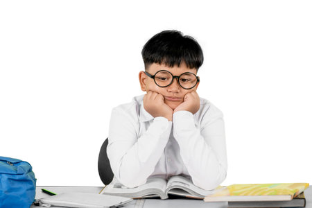 Bored Schoolboy with Glasses Sitting at Desk with Open Books and Backpack on White Background