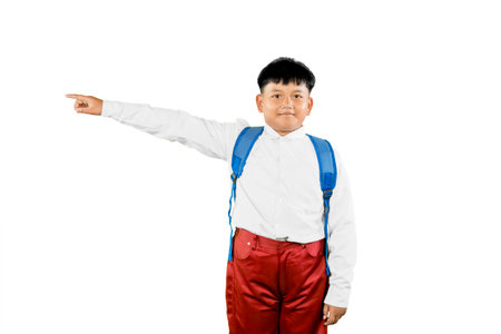 Indonesian Elementary School Boy Pointing Sideways in Uniform with Backpack Isolated on Whiteの写真素材