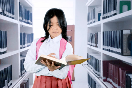 Asian Schoolgirl Reading a Book in the Library While Wearing Uniform and Backpack