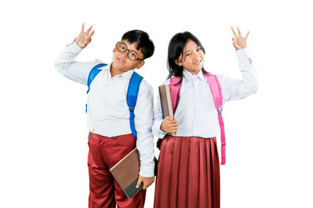 Cheerful Indonesian Schoolchildren Waving and Holding Books Isolated on White Backgroundの写真素材