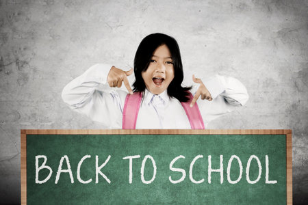 Excited schoolgirl pointing at 'Back to School' message on green chalkboard