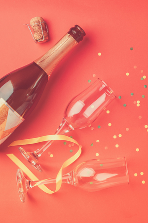 A bottle of champagne and glasses on a fashionable coral background. Festive concept. Vertical frame. Copy space. Flat layout.の写真素材