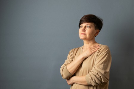 Middle-aged woman posing standing near the wall. Woman portrait on a gray background. Copy space.の写真素材