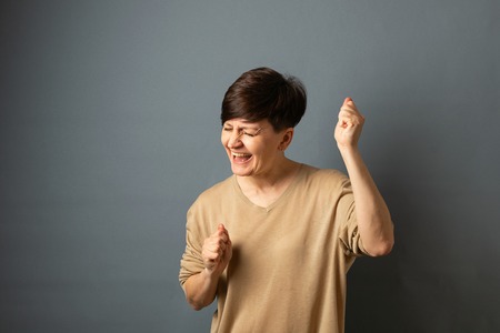 A woman screams rejoices posing by the wall. Woman portrait on a gray background. Copy space.の写真素材