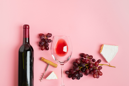 A bottle of wine an empty glass a bunch of grapes slices of cheese on a gentle pink background. Minimalism. Top viewの写真素材