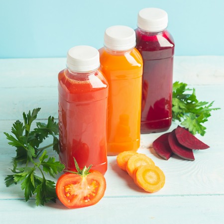 Fresh juice smoothies from a variety of vegetables carrots apple tomatoes beets in bottles on a wooden blue background.の写真素材