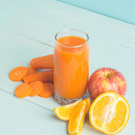 Fresh juice from carrots and orange apples in a glass on a wooden blue background. Selective focus. Copy space.の写真素材