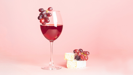 A glass with red wine and snack on a delicate pink background. Selective focus. Copy space. Minimalismの写真素材
