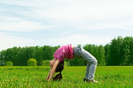 Little girl does yoga gymnastics on a green meadow in the park. Summer concept, childrens games in...