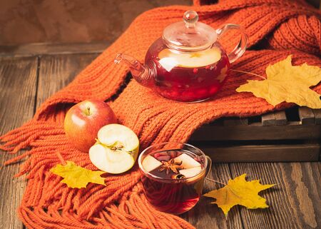 Drink autumn apple red berries in a glass teapot and an orange scarf on a wooden background. Hot fruit berry tea.の写真素材