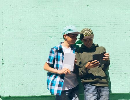 Two teen boys stand with a mobile phone or smartphone against a green wall. School concept. Copy space.の写真素材