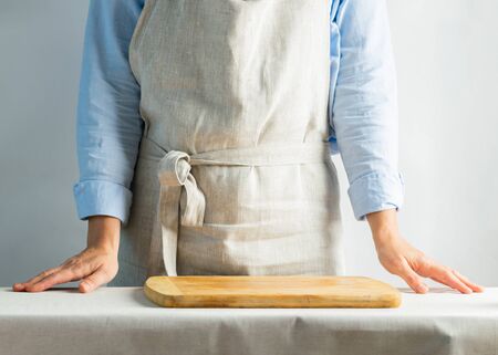 Female cook in cotton apron at the kitchen table with cutting board. Rustic natural style. Kinfolk...