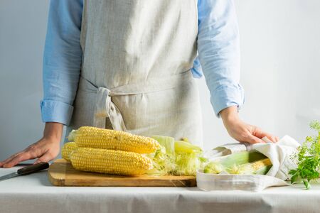 Woman cook in cotton apron holds ripe corn in her hands. Rustic natural style. The concept organic food. Kinfolk style.の写真素材