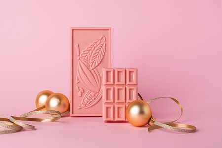 Chocolate pink tiles on a gentle pastel background and golden Christmas toys. Front view. Concept...