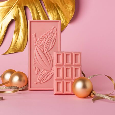 Chocolate pink tiles on a delicate pastel background and golden Christmas toys plant leaf. Festive...