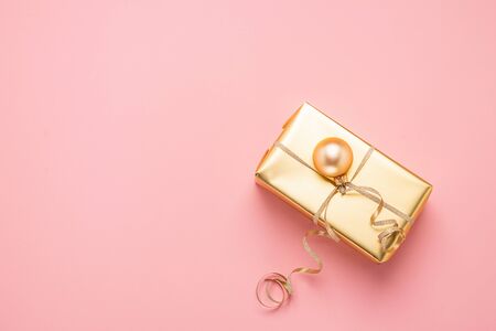 Festive box with festive ribbon golden toy balls on a pastel pink background. Flat style layout. Holiday concept. Copy space. Horizontal frameの写真素材