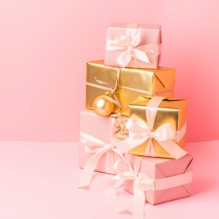 Festive golden pink boxes with satin ribbon bow toy balls on a pastel pink background. Holiday concept. Square frameの写真素材