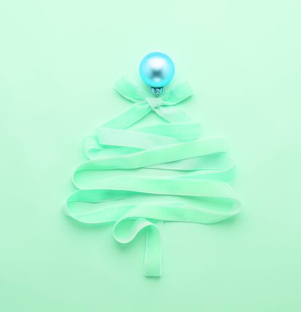 Christmas creative tree made of ribbon decorated with a golden ball on a pastel mint neon background. Festive minimalism concept. Flat style layout. Copy space. Square frameの写真素材