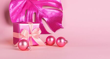 Festive box with a satin bow and golden neon toy balls on a pastel pink background . Holiday concept. Copy spaceの写真素材