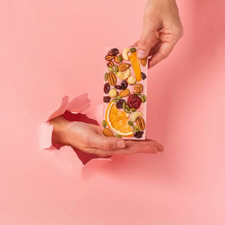 Chocolate pink bar holds a female hand on a pink background burst paper hole. Food concept art....