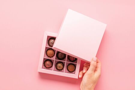 Female hand opens a box with sweets pink background . Gifts festive food love concept. Horizontal...