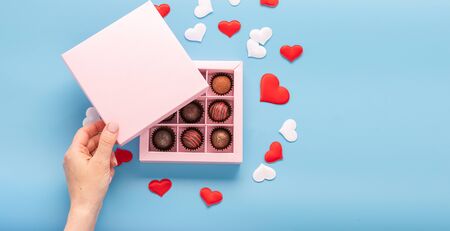 Female hand opens a box with chocolates blue background with hearts. Valentines day concept festive food gifts.の写真素材