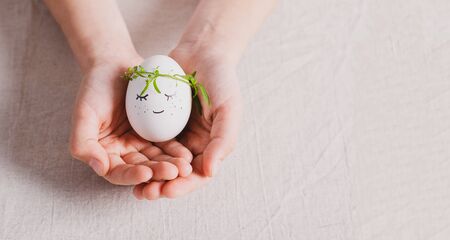 Festive composition Easter egg with a funny muzzle with eyes in the hands of child. Happy easter concept.selective focusの写真素材