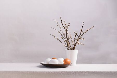 Festive Easter eggs in clay plate of willow twigs on a table. Light background Happy Easter concept. Horizontal frameの写真素材