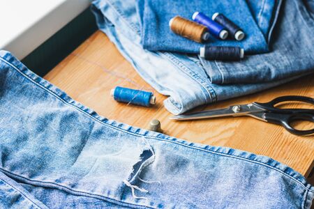 Handicraft, repair and tailoring. Sewing accessories threads close-up denim on a wooden table. Horizontal frame copy spaceの写真素材