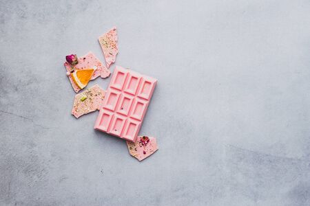 Chocolate pink whole bar decorated with slices of fruits nuts and slices gray background....