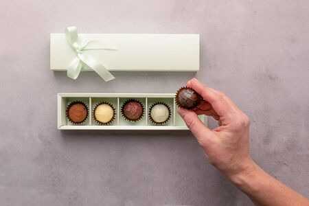 A girl holds a box of chocolates on gray background. Flat layout top view. Horizontal frame copy...