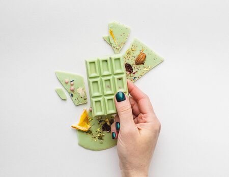 A female hand with bright manicure holds chocolate colored tiles with the addition of pistachios on...