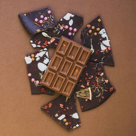 Dark milk chocolate whole bar decorated with pieces of fruit nuts and slices brown background. Minimalism is monochrome.の写真素材