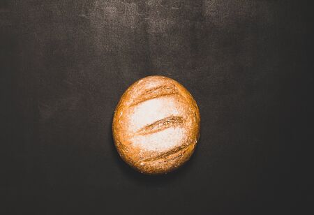 One bun of freshly baked bread on a black background. The concept of minimalism food. Flat layoutの写真素材