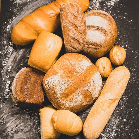 Fresh baked bread with a golden crust, loaf, buns, white, rye on a rustic wooden background with sil...