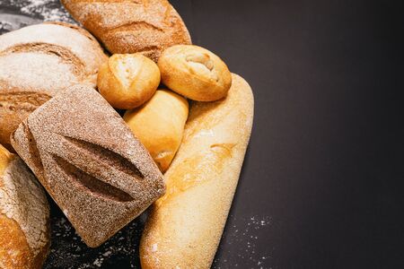 Assortment of fresh baked bread with a golden crust a black rustic background. Flat layout with...
